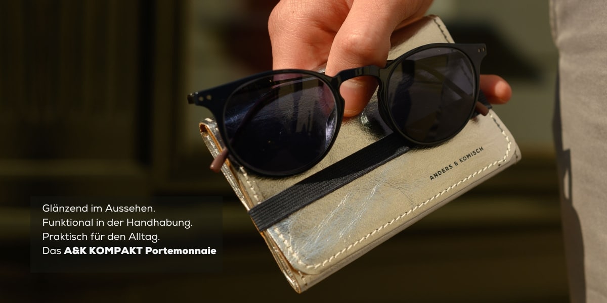 Kompaktes mittelgroßes Portemonnaie für Damen und Herren in Silber. Zum Größenvergleich trägt der Mann einen Sonnenbrille in der Hand.